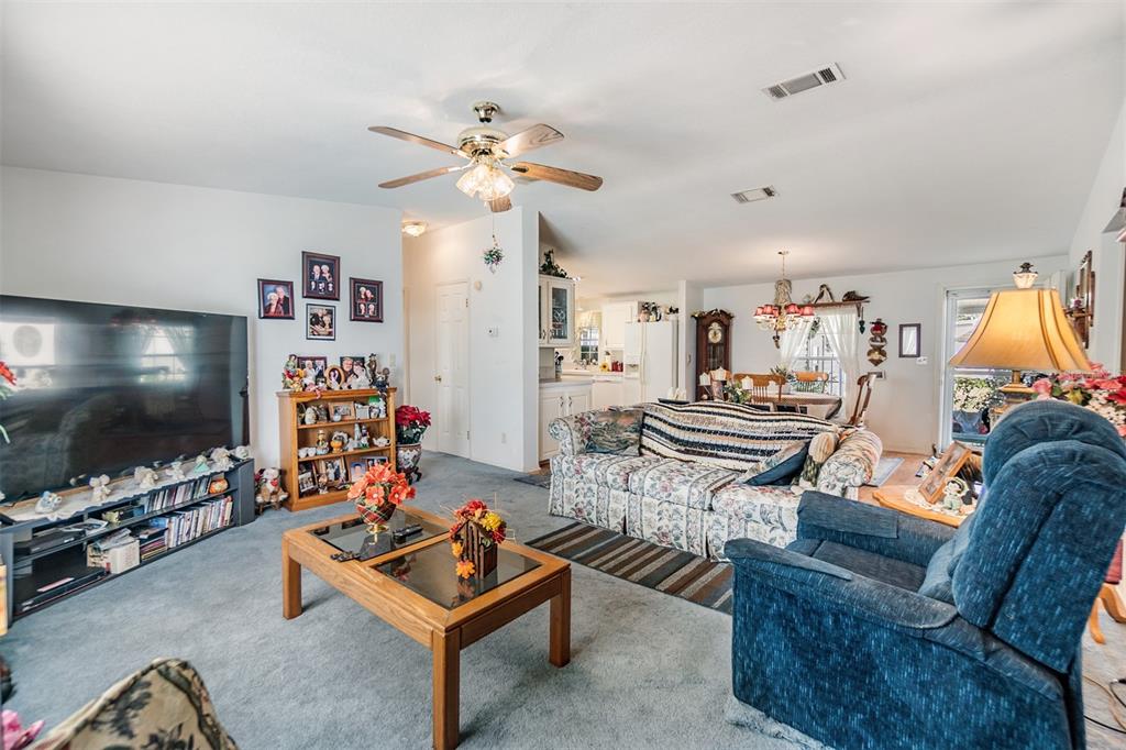 A living room with a floral sofa, blue recliner, coffee table, and television — 37340 NEUKOM AVENUE, ZEPHYRHILLS, FL