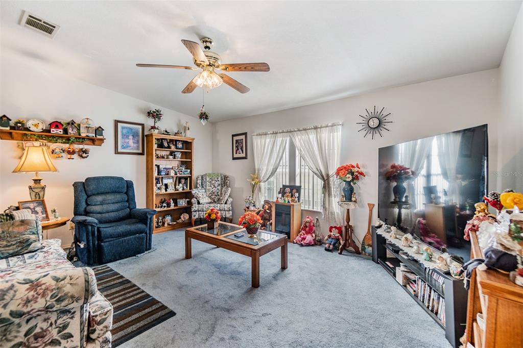 A living room features a blue recliner, a wooden coffee table, and a large television — 37340 NEUKOM AVENUE, ZEPHYRHILLS, FL