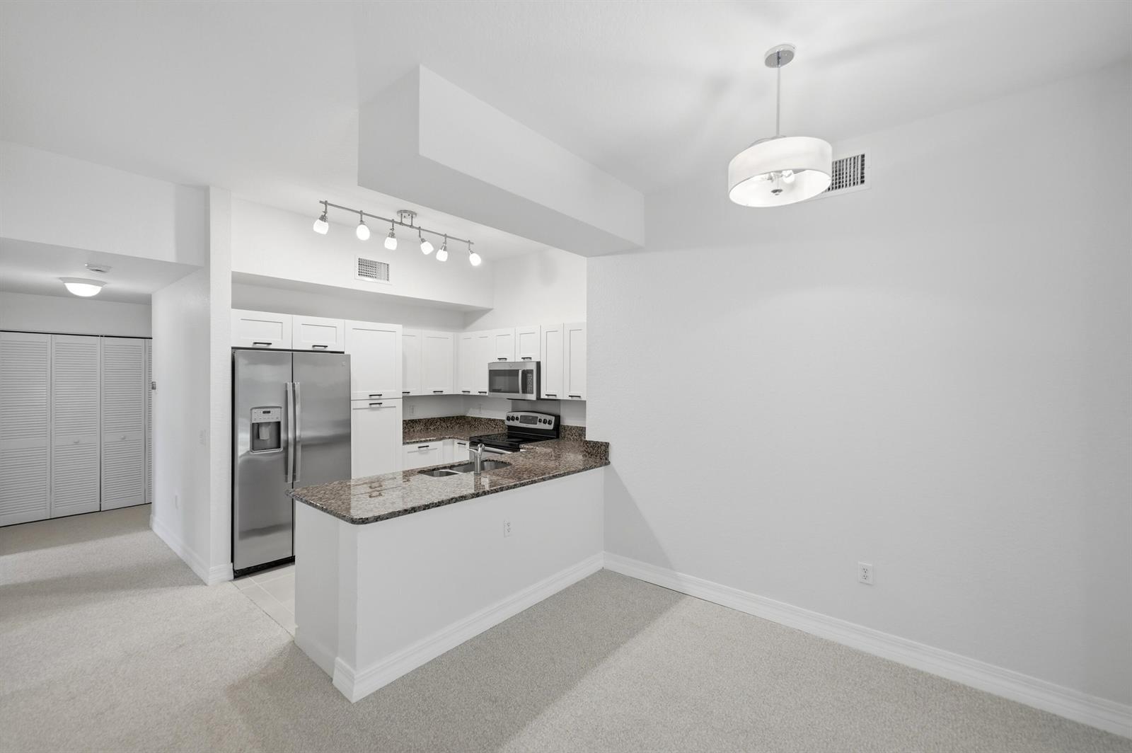 A kitchen with white cabinets, granite countertops, and stainless steel appliances opens to a dining area — 58 SE Palermo Court # 104, Stuart FL 34994, STUART, FL