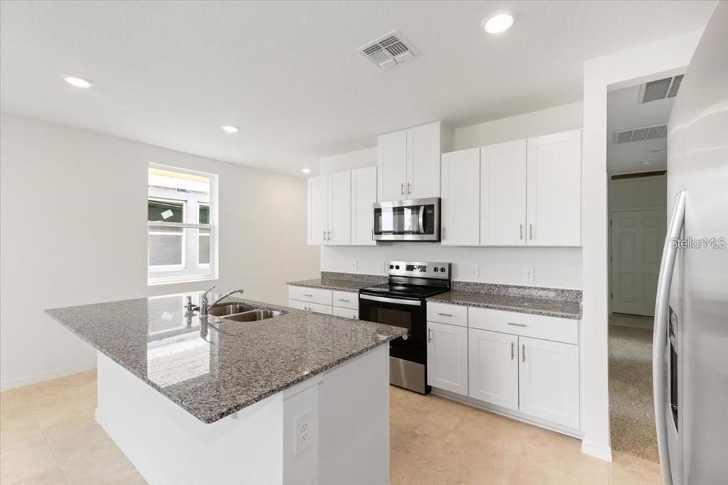 A kitchen features white cabinets, granite countertops, a center island, and stainless steel appliances — 1361 CURRENT PLACE, HAINES CITY, FL