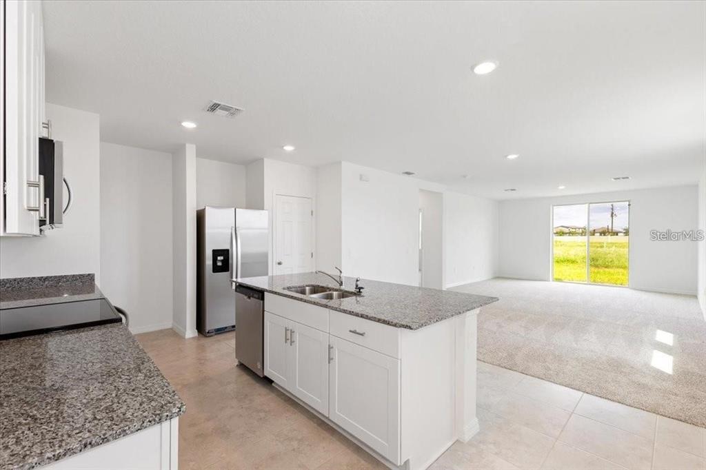 A kitchen with white cabinets and granite countertops opens to a carpeted living area — 1361 CURRENT PLACE, HAINES CITY, FL
