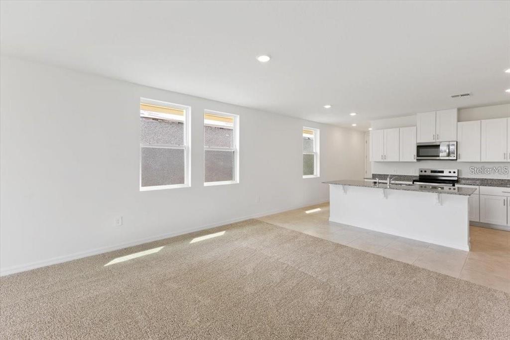 An open-concept living room with beige carpeting transitions into a kitchen with white cabinetry — 1361 CURRENT PLACE, HAINES CITY, FL