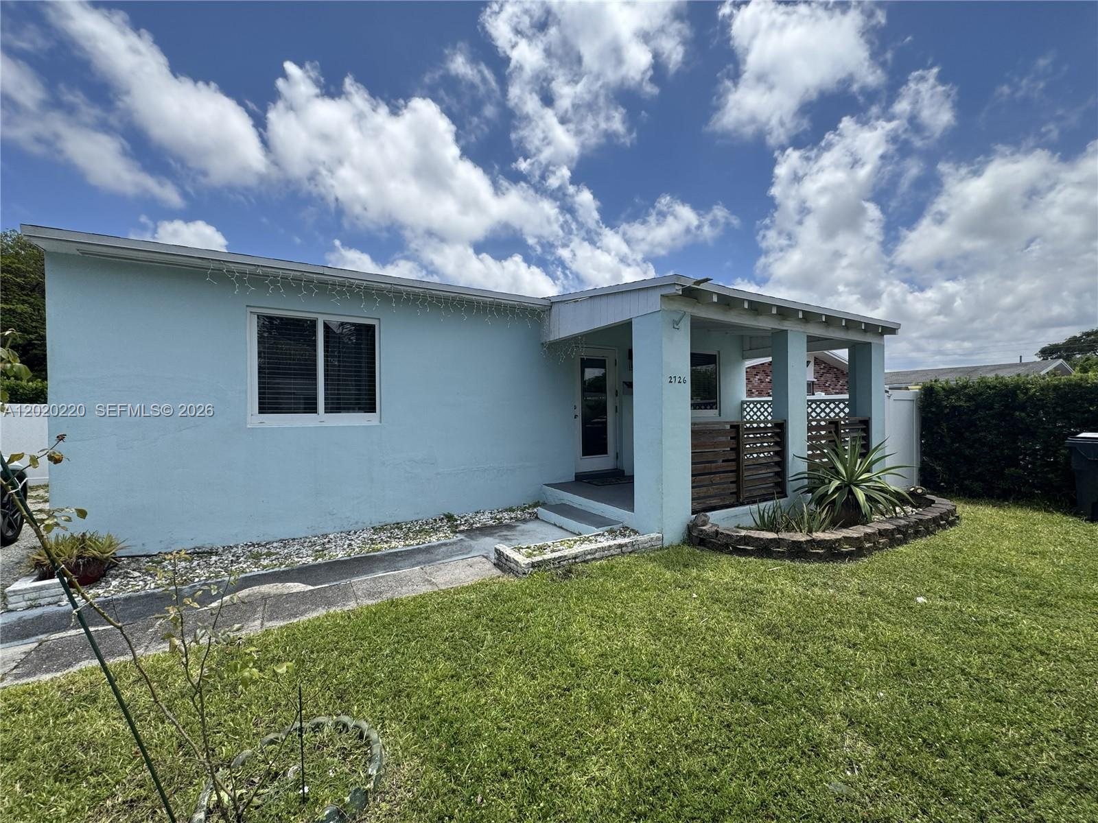 A light blue single-story house features a covered front porch with wooden lattice railings — 2726 Taylor St, Hollywood FL 33020, HOLLYWOOD, FL