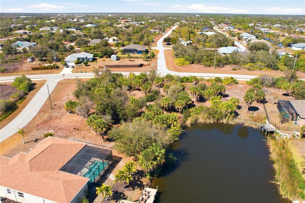 An aerial view shows a vacant lot with trees and a pond near houses — 9882 CALUMET BOULEVARD, PORT CHARLOTTE, FL