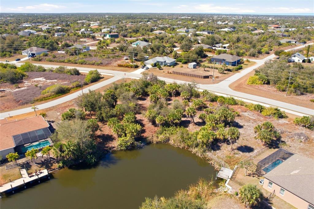 An aerial view shows a vacant lot with vegetation situated between two houses and a pond — 9882 CALUMET BOULEVARD, PORT CHARLOTTE, FL