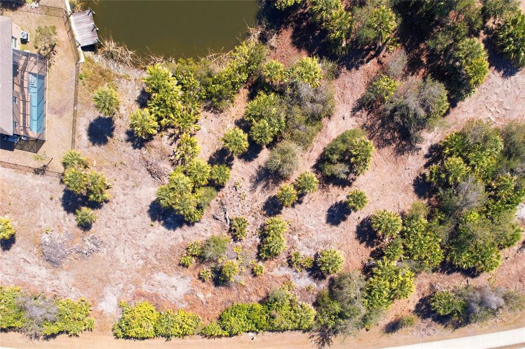 An aerial view shows a vacant, wooded lot with a small pond and adjacent house — 9882 CALUMET BOULEVARD, PORT CHARLOTTE, FL