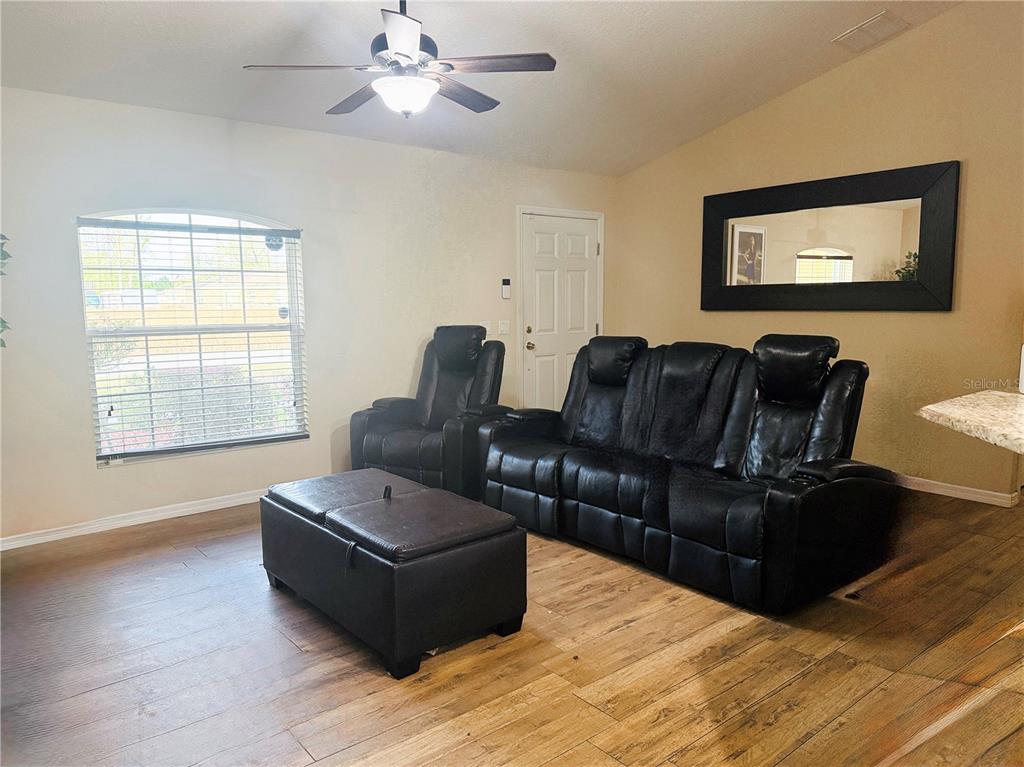 A living room features wood-look flooring, a black leather sofa and recliner, and a ceiling fan — 36 WALNUT COURSE, OCALA, FL