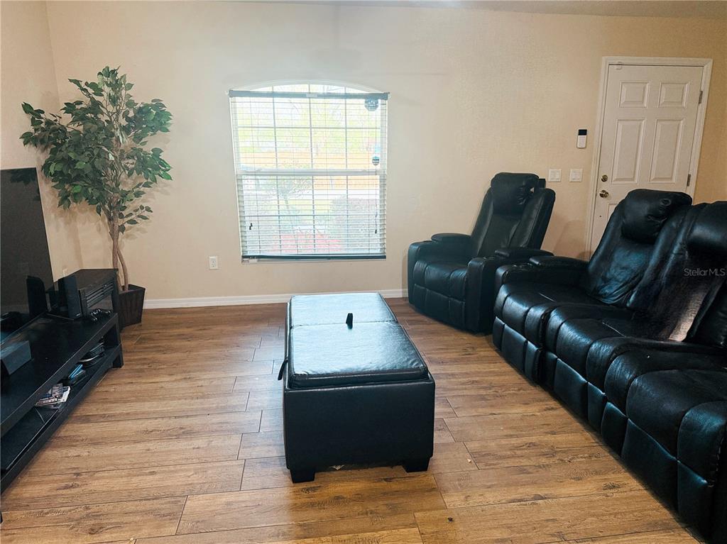 A living room features wood-look flooring, a black leather sofa, a recliner, and a window — 36 WALNUT COURSE, OCALA, FL