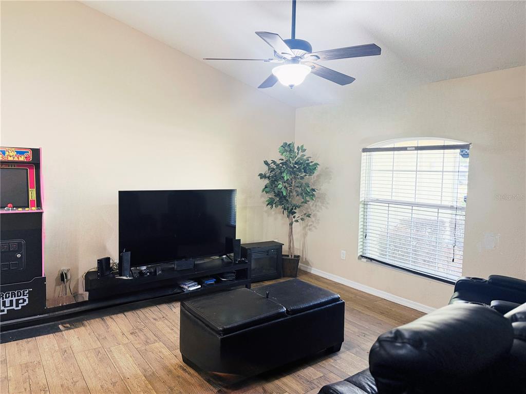 A living room features a television, an arcade cabinet, a ceiling fan, and wood-look flooring — 36 WALNUT COURSE, OCALA, FL