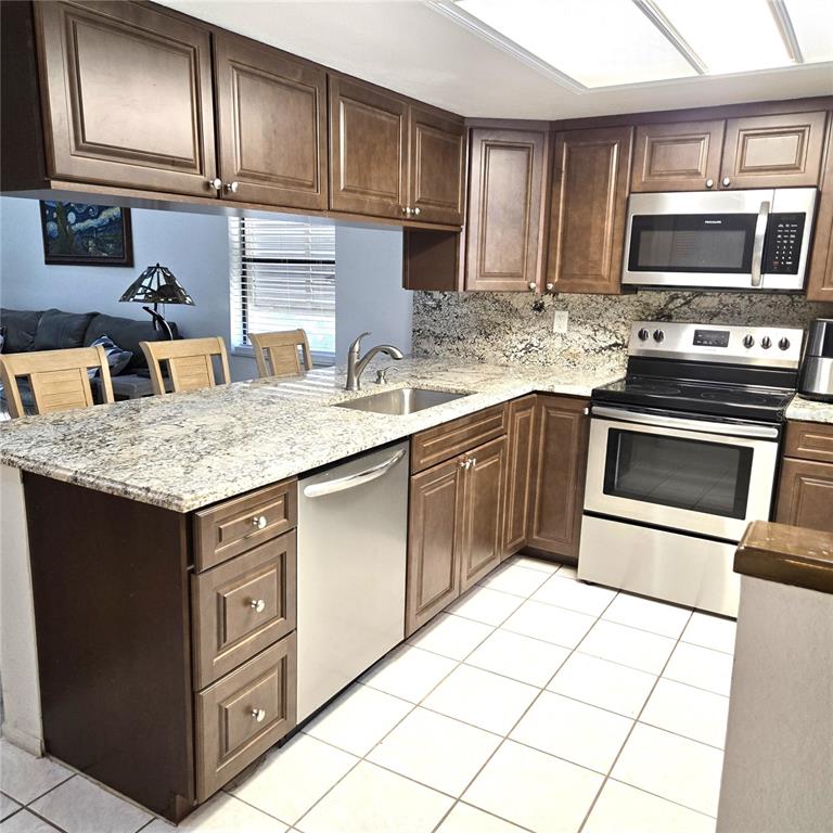 A kitchen features dark wood cabinets, granite countertops, stainless steel appliances, and white tile flooring — 302 40TH STREET CIRCLE W, PALMETTO, FL