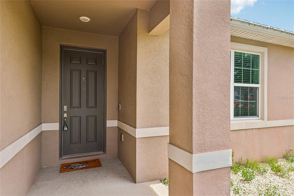 A tan stucco home exterior features a dark brown front door and a square pillar — 5277 SE 91ST PLACE, OCALA, FL
