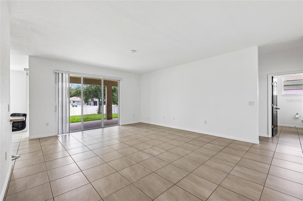 An empty living room features light-colored tile flooring, white walls, and sliding glass patio doors — 5277 SE 91ST PLACE, OCALA, FL