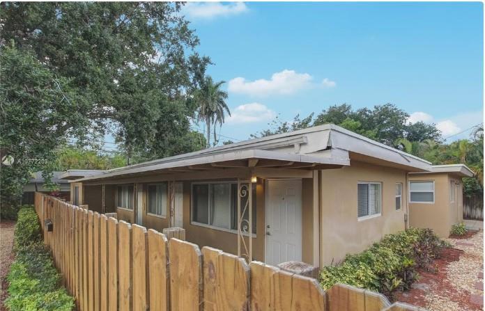A single-story tan building with a wooden fence and palm trees under a blue sky — FORT LAUDERDALE, FL