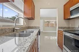 A kitchen features granite countertops, a stainless steel sink, wood cabinets, and a microwave — FORT LAUDERDALE, FL