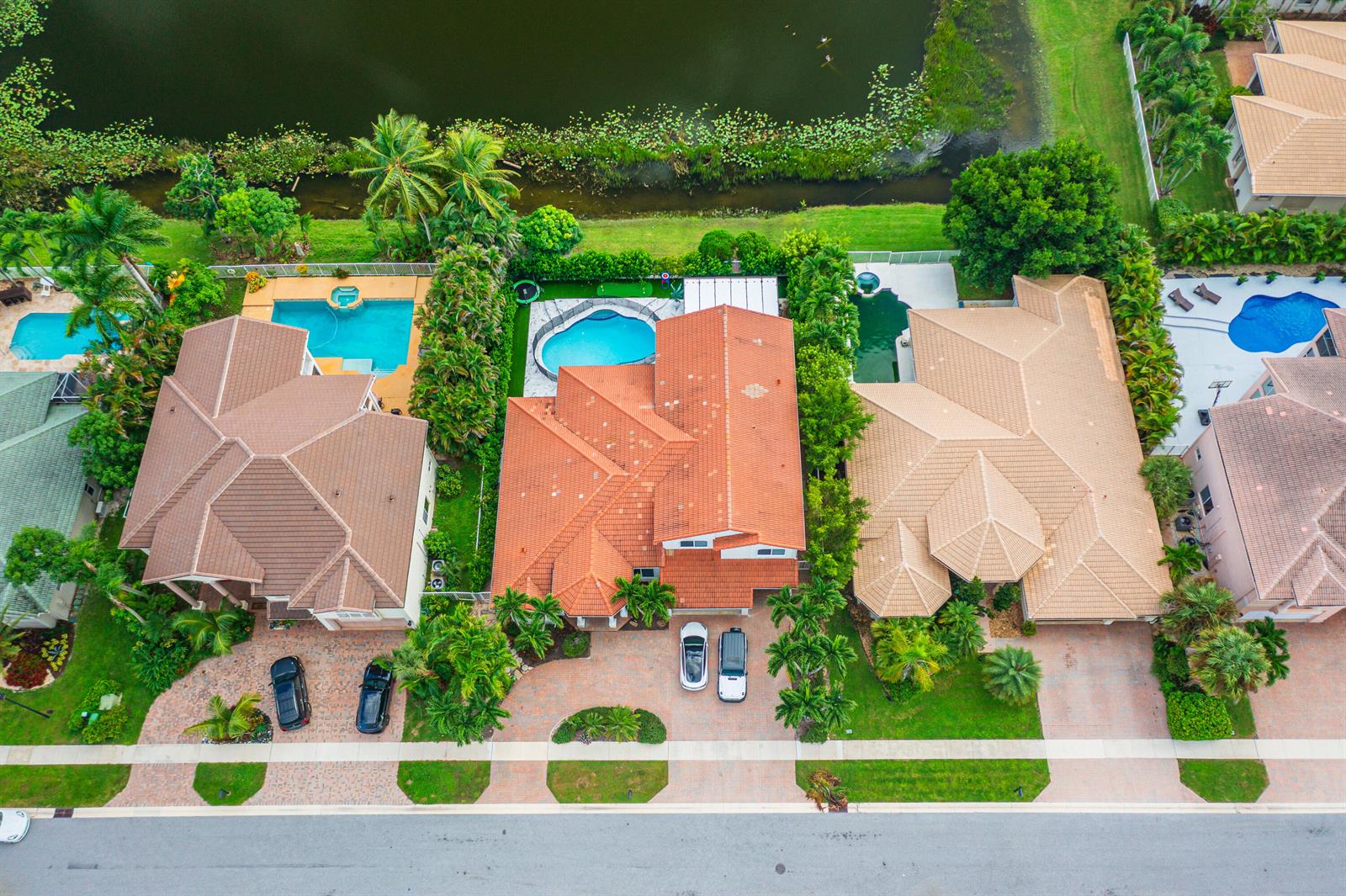 An aerial view shows three suburban houses with swimming pools and tile roofs near a lake — 11804 Osprey Pointe Circle, Wellington FL 33449, WELLINGTON, FL