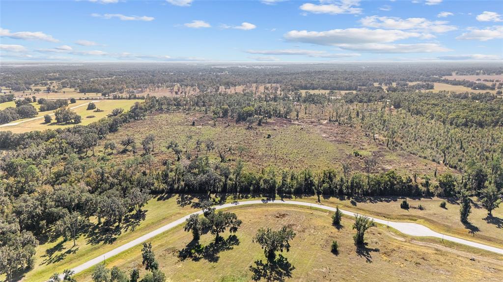 An aerial view shows a large, partially cleared grassy lot bordered by trees and roads — 1 PETITION UNIT 4261-1, OCALA, FL