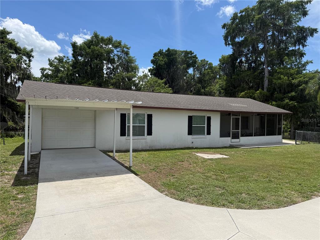 A single-story white house features a carport, a screened porch, and a concrete driveway — 1141 COUNTY ROAD 457, LAKE PANASOFFKEE, FL