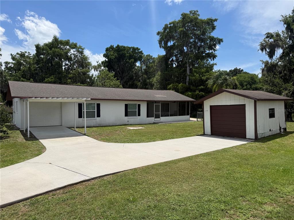 A white single-story house with a carport and a detached garage on a grassy lot — 1141 COUNTY ROAD 457, LAKE PANASOFFKEE, FL