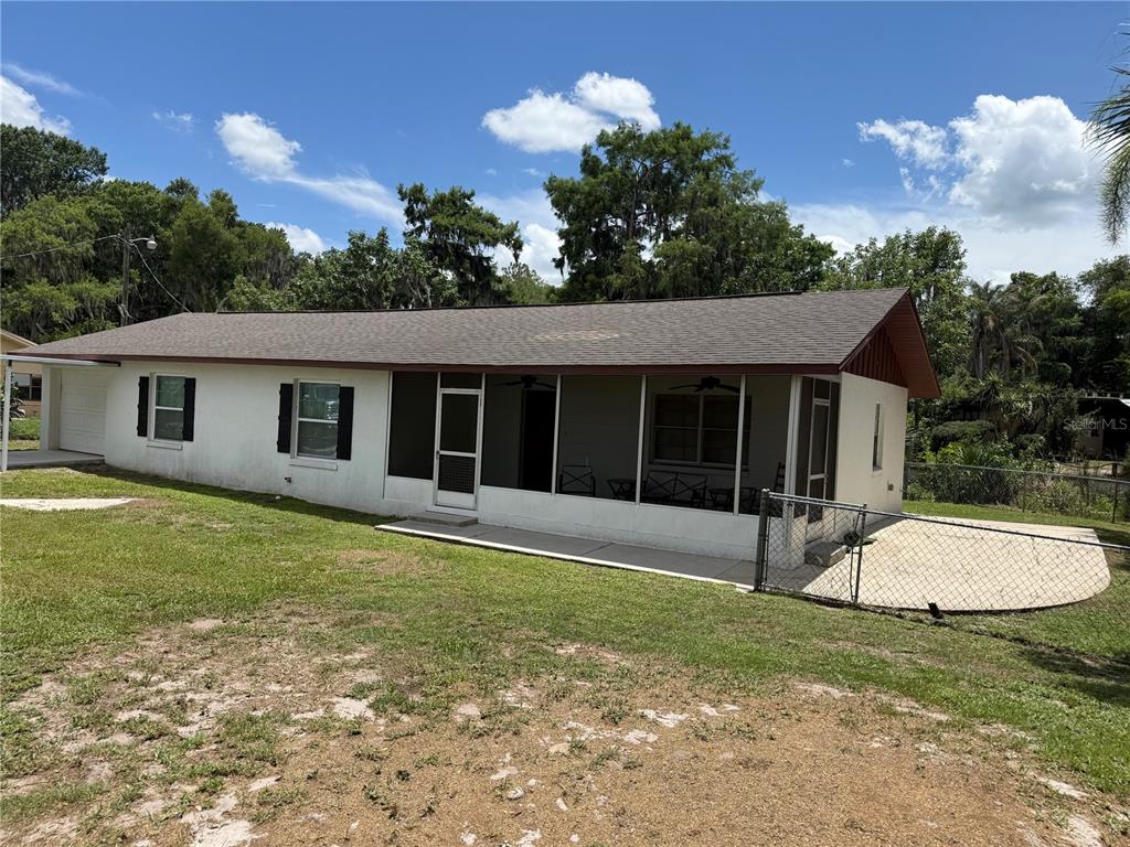A single-story house with a screened-in porch, white stucco walls, and a brown shingled roof — 1141 COUNTY ROAD 457, LAKE PANASOFFKEE, FL