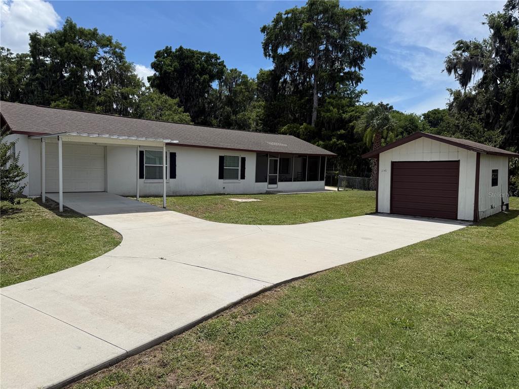 A single-story house with a carport and a detached garage sits on a grassy lot — 1141 COUNTY ROAD 457, LAKE PANASOFFKEE, FL