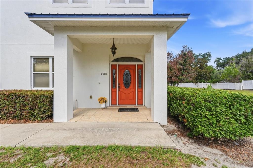 A covered porch leads to a bright orange front door with sidelights and a transom window — 1415 NEW JERSEY ROAD, LAKELAND, FL