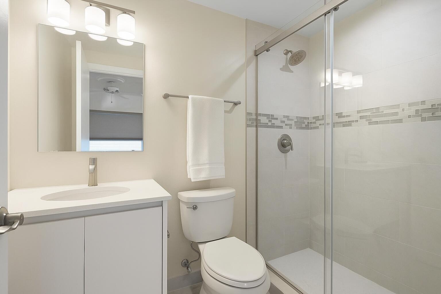 A modern bathroom features a white vanity, a toilet, and a glass-enclosed walk-in shower — 3401 Spanish Trail # 151, Delray Beach FL 33483, DELRAY BEACH, FL