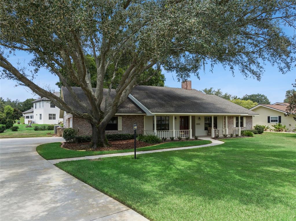 A single-story brick and siding house with a large oak tree and front porch — 34035 PARK LANE, LEESBURG, FL