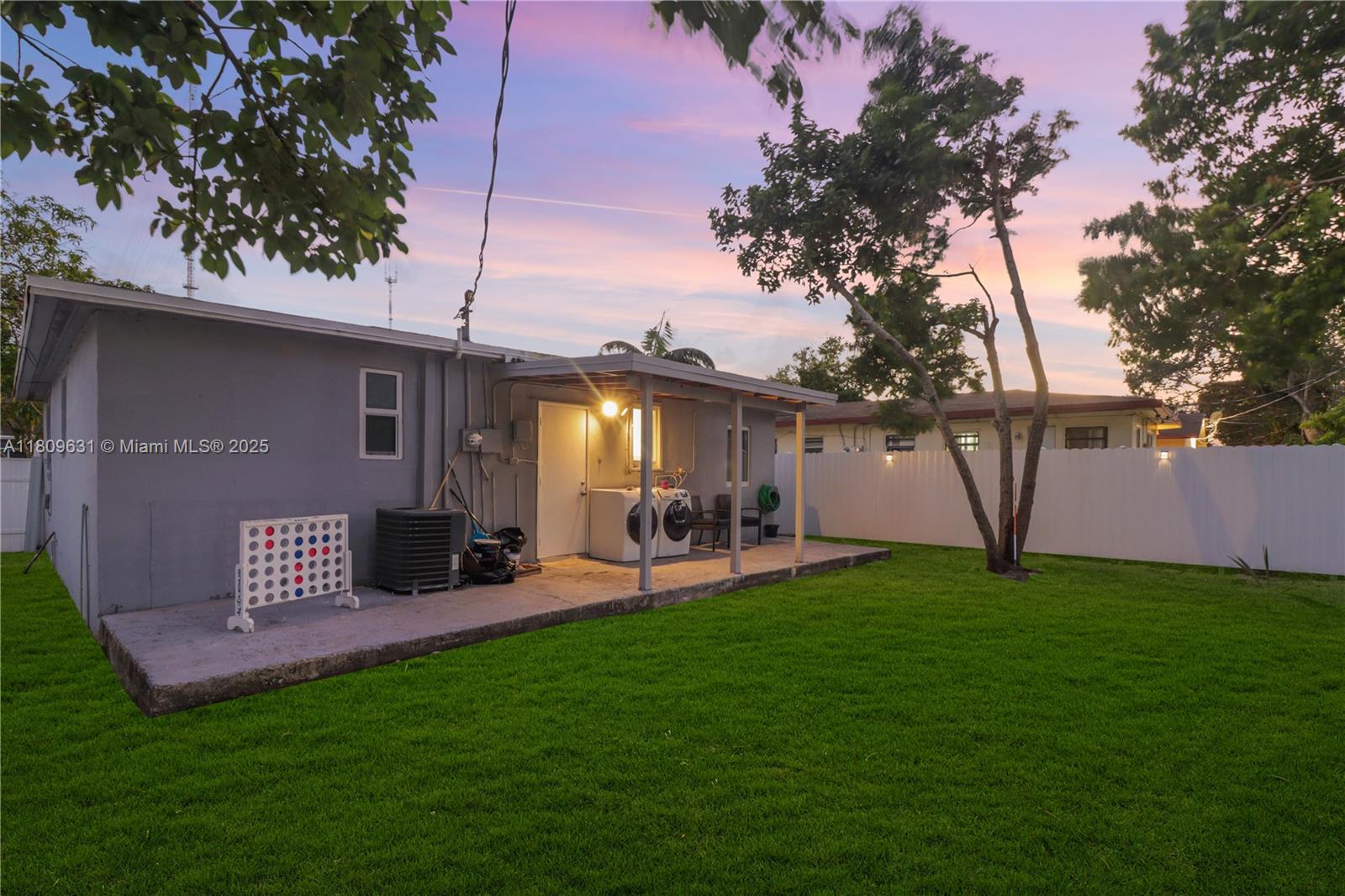 A gray house exterior features a covered concrete patio with laundry appliances and a lawn — 6039 SW 38th St, Miramar FL 33023, MIRAMAR, FL