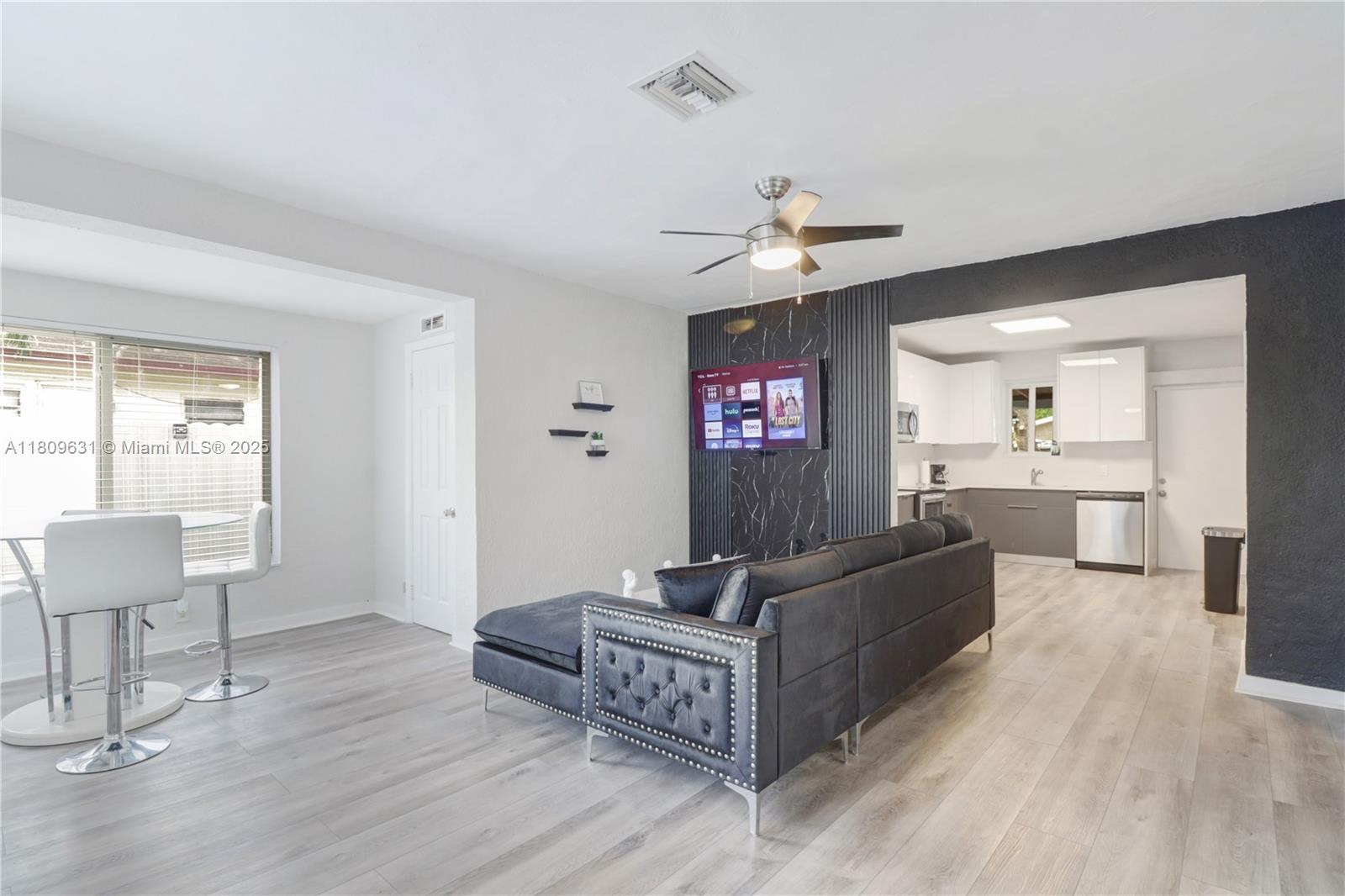A living room with a dark tufted sofa, marble-look accent wall, and adjacent kitchen area — 6039 SW 38th St, Miramar FL 33023, MIRAMAR, FL