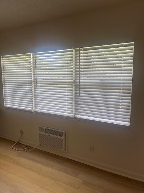 A room with light wood flooring, white horizontal blinds on three windows, and a wall-mounted AC — 90 Mansfield C, Boca Raton FL 33434, BOCA RATON, FL