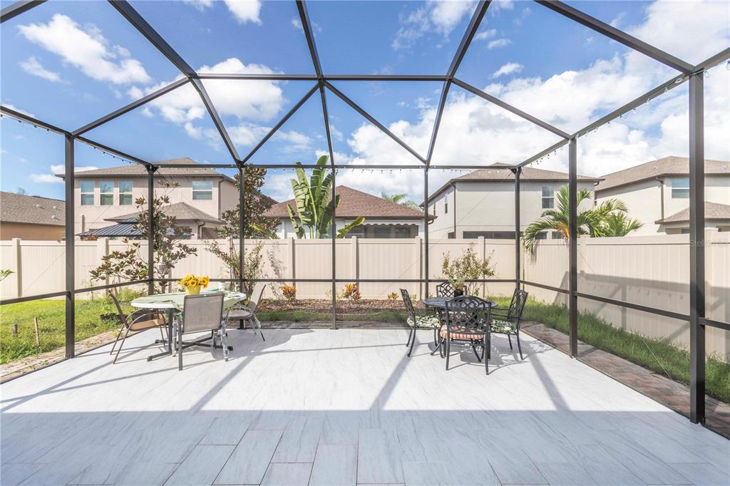 A screened-in patio features light-colored tile flooring, two dining sets, and a vinyl privacy fence — 8585 WINNING FIELDS ROAD, NEW PORT RICHEY, FL