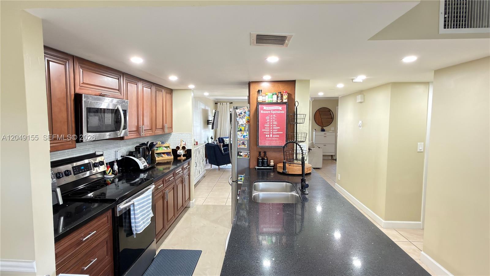 A kitchen features dark wood cabinets, black countertops, a stainless steel microwave, and an island — 9492 NW 39th St, Sunrise FL 33351, SUNRISE, FL