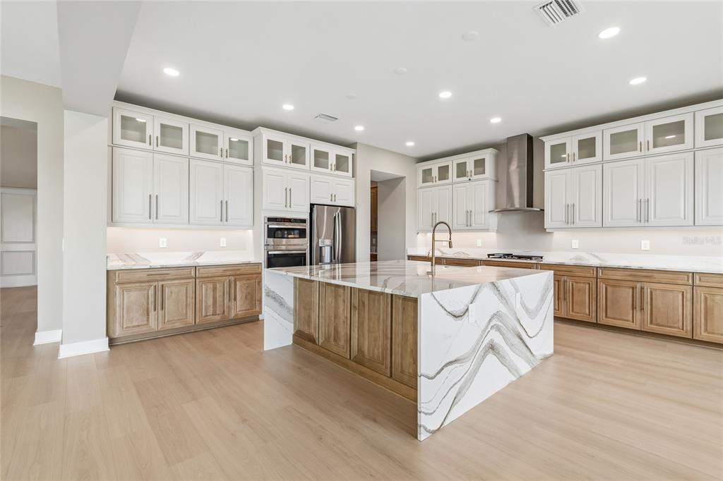 A modern kitchen features two-toned cabinetry, a large waterfall island, and light wood flooring — 1170 KINGS WAY DRIVE, NOKOMIS, FL
