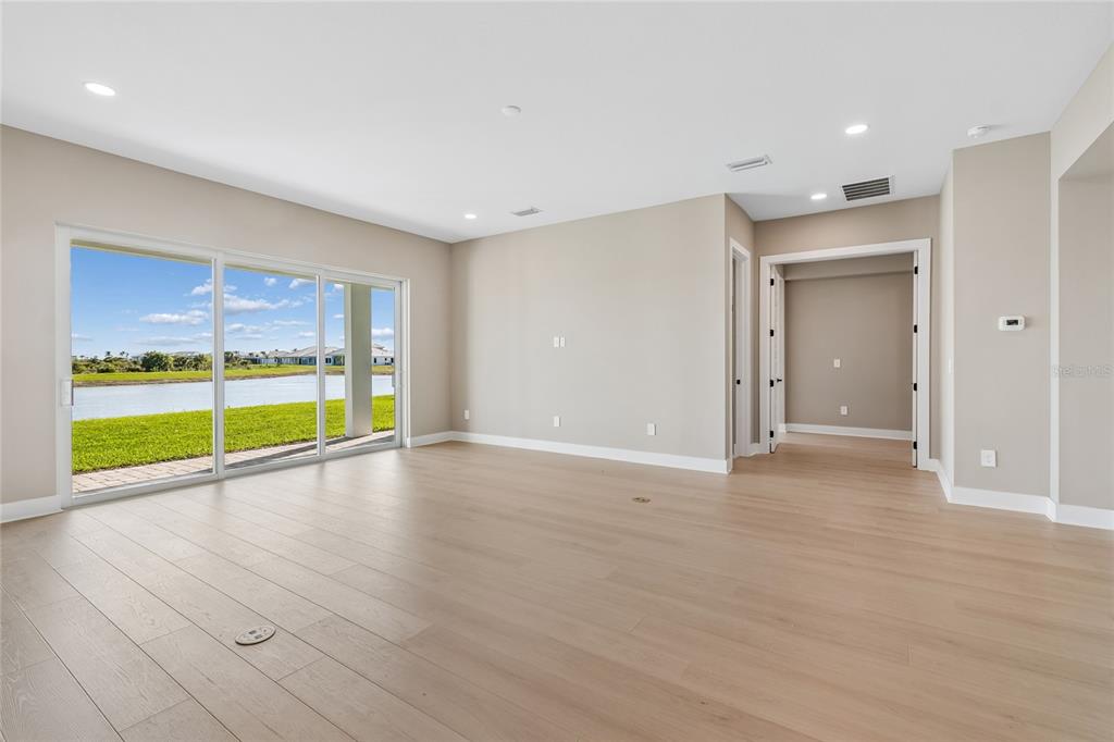 An empty living room with light wood floors, recessed lighting, and sliding doors overlooking a lake — 1170 KINGS WAY DRIVE, NOKOMIS, FL