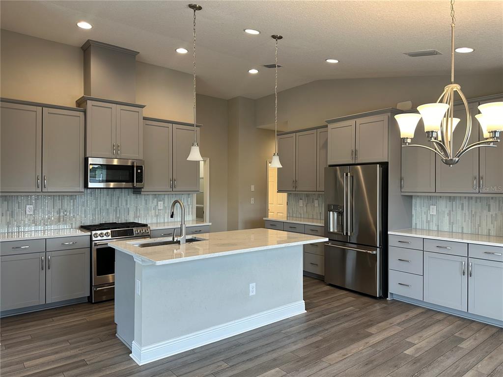 A modern kitchen features gray cabinets, stainless steel appliances, a center island, and tile backsplash — 12573 OAK HILL WAY, PARRISH, FL