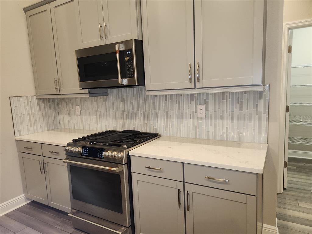 A kitchen features gray cabinets, stainless steel appliances, a white countertop, and a tiled backsplash — 12573 OAK HILL WAY, PARRISH, FL