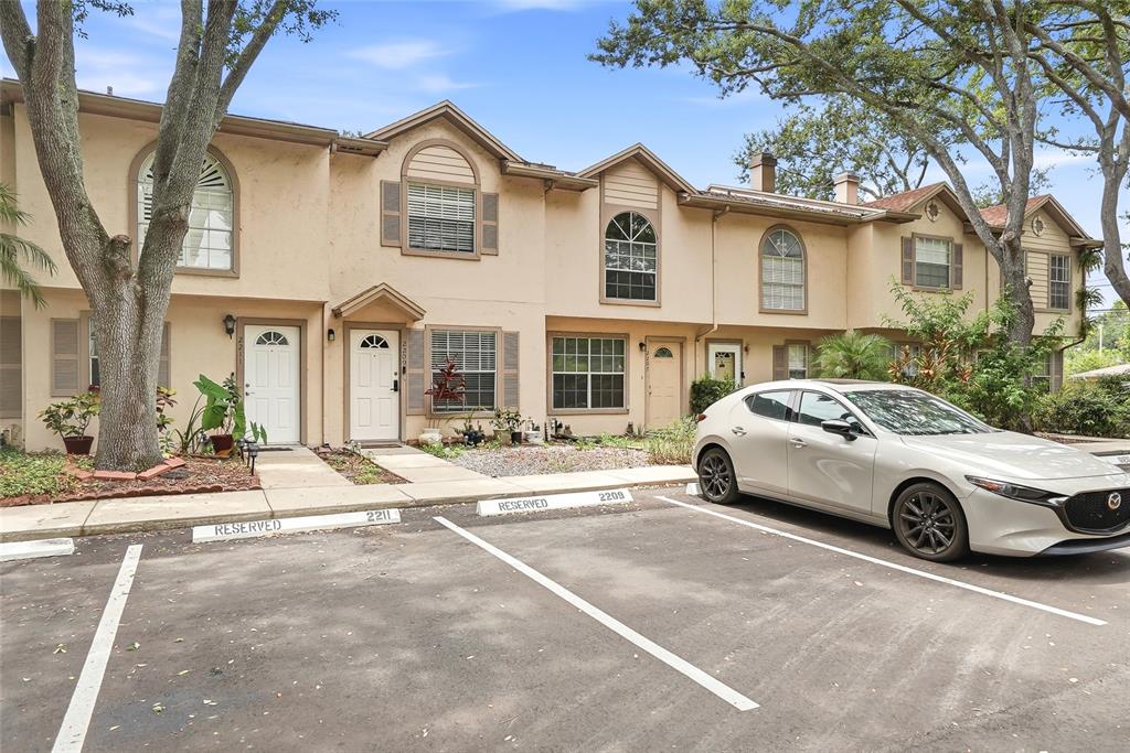 A row of two-story townhouses with tan stucco siding and reserved parking spaces in front — 2209 FLETCHERS POINT CIRCLE, TAMPA, FL
