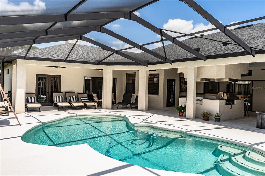 A screened-in patio features a swimming pool, lounge chairs, and an outdoor kitchen area — 2205 CHESTERFIELD CIRCLE, LAKELAND, FL