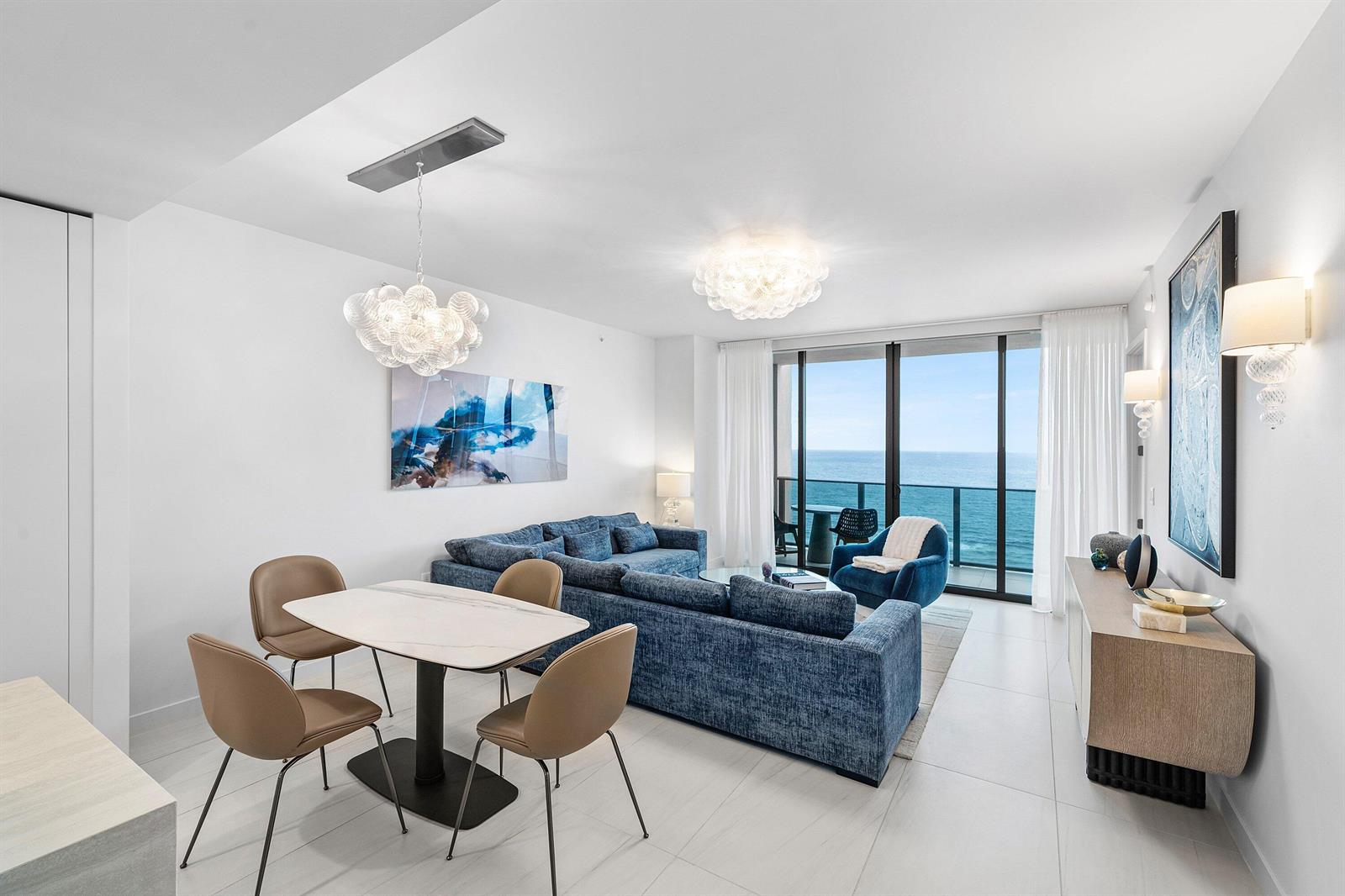 A modern living and dining area features blue furniture, a marble table, and ocean views — 900 N Ocean Boulevard # 1504, Pompano Beach FL 33062, POMPANO BEACH, FL