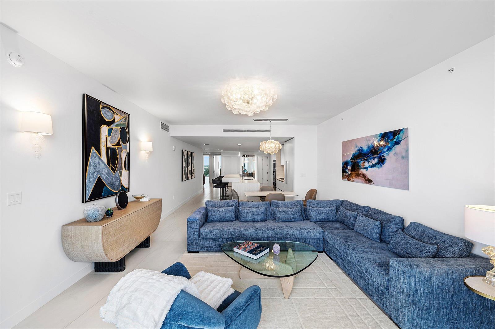 A modern living room features a large blue sectional sofa, glass coffee table, and artwork — 900 N Ocean Boulevard # 1504, Pompano Beach FL 33062, POMPANO BEACH, FL