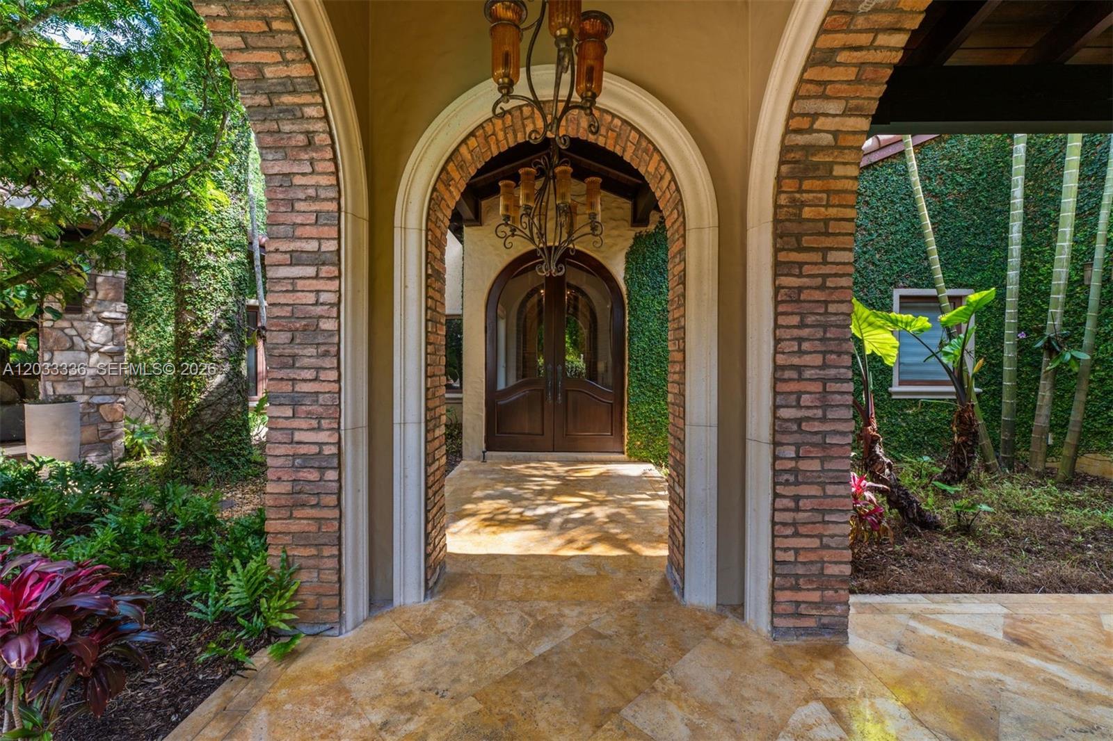 An arched brick entryway leads to a wooden double door with a hanging chandelier — 6201 SW 96th St # 0, Pinecrest FL 33156, PINECREST, FL