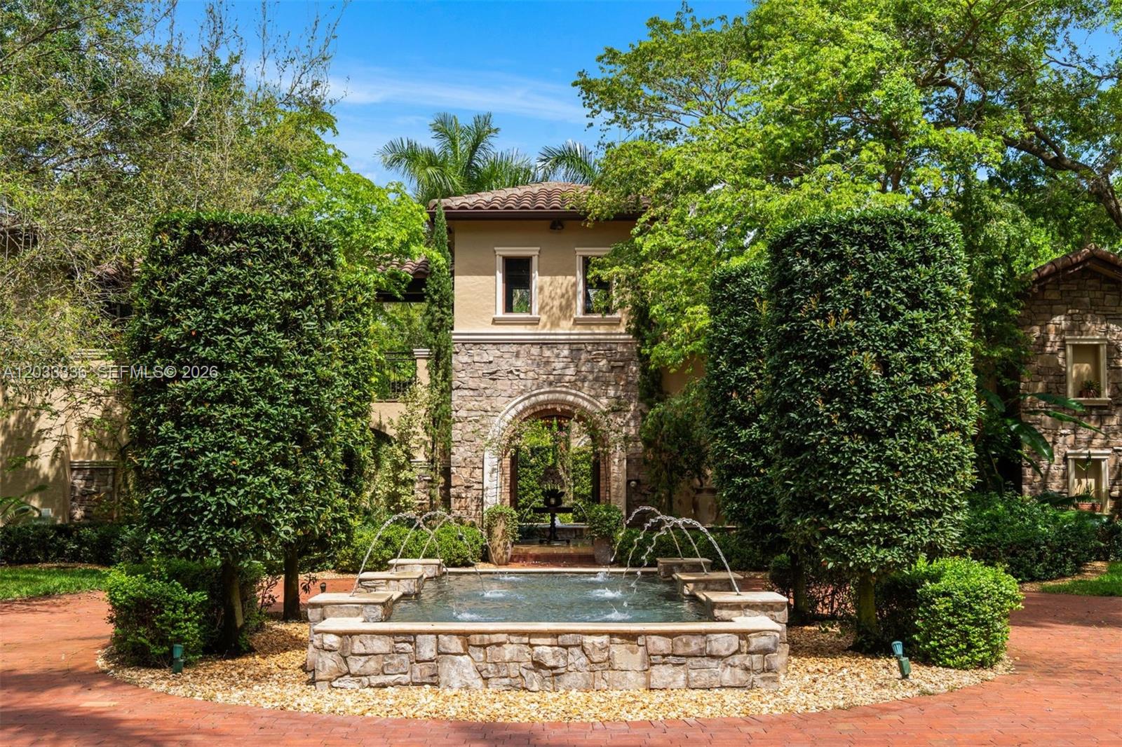 A stone fountain sits in front of a Mediterranean-style home with an arched entryway — 6201 SW 96th St # 0, Pinecrest FL 33156, PINECREST, FL