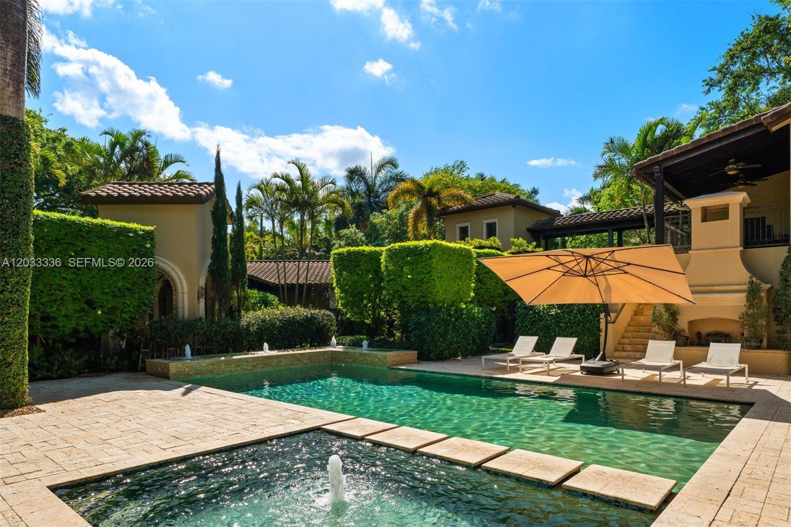 A swimming pool with a fountain and lounge chairs sits in a landscaped backyard patio — 6201 SW 96th St # 0, Pinecrest FL 33156, PINECREST, FL