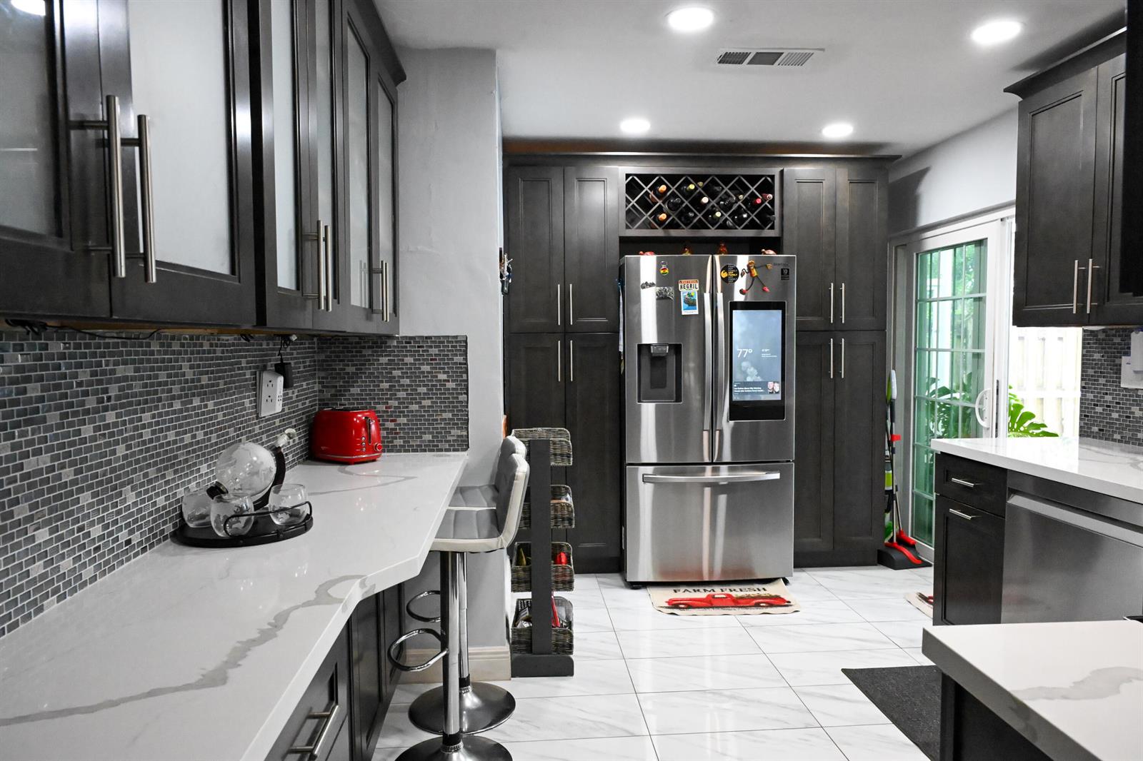 A modern kitchen features dark cabinetry, white marble-style countertops, stainless steel appliances, and tiled flooring — 8610 NW 27th Place, Sunrise FL 33322, SUNRISE, FL