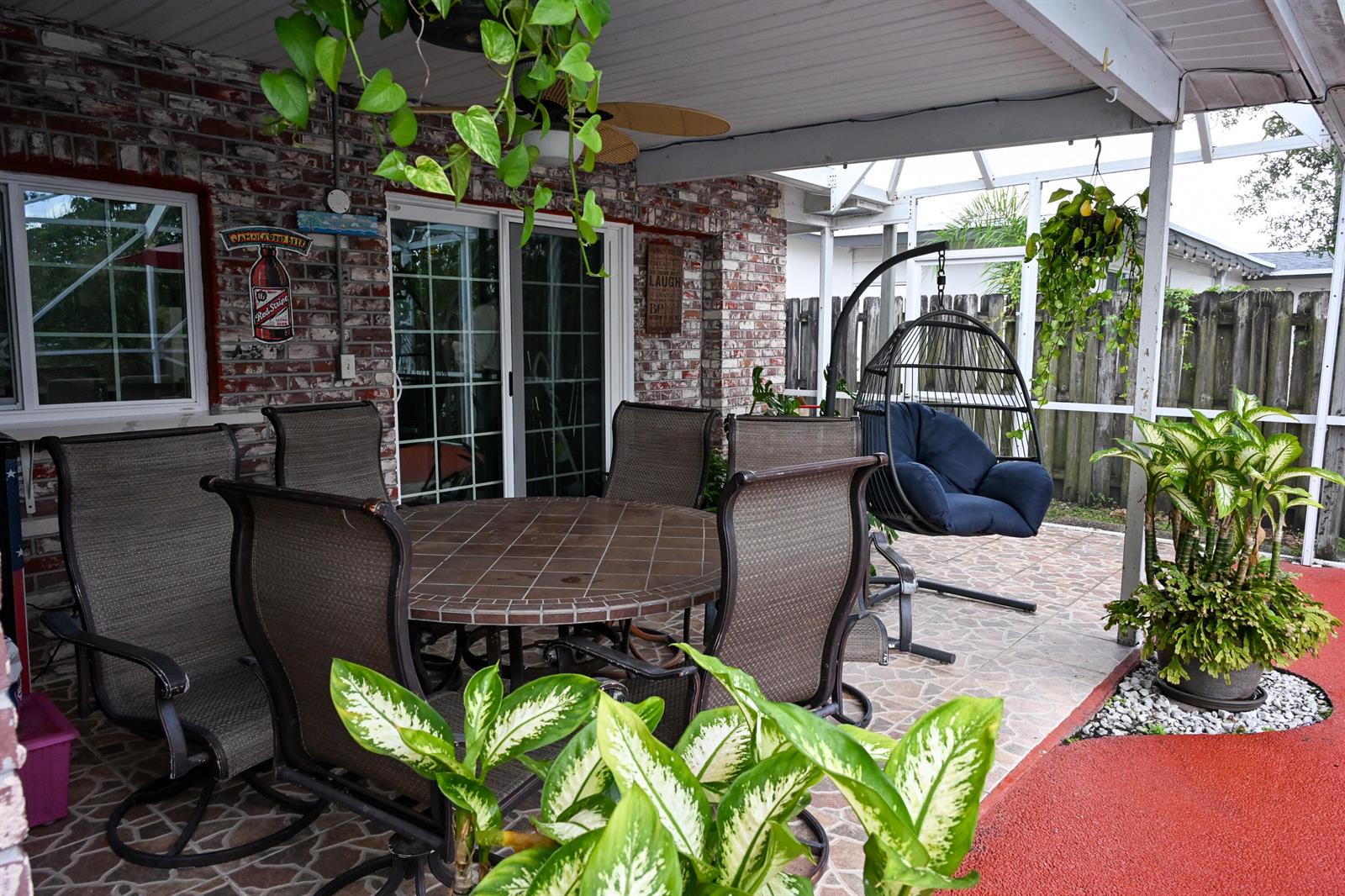 A covered patio features a tiled dining set, a hanging egg chair, and potted plants — 8610 NW 27th Place, Sunrise FL 33322, SUNRISE, FL