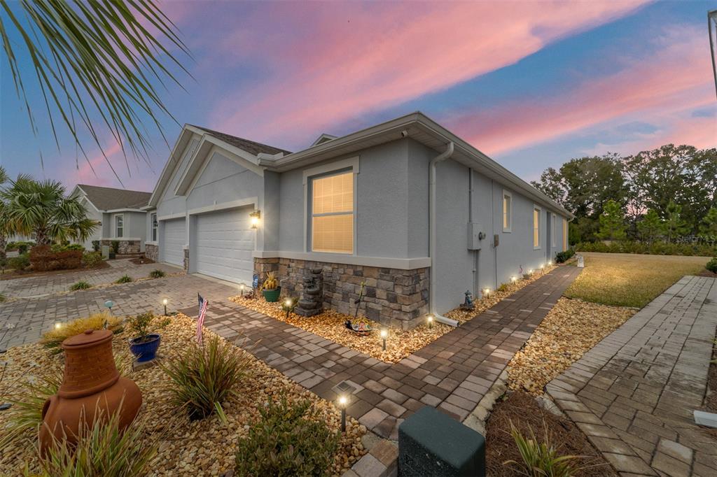 A gray house with a stone facade, paver walkway, and garage at sunset — 5361 NW 48TH PLACE, OCALA, FL