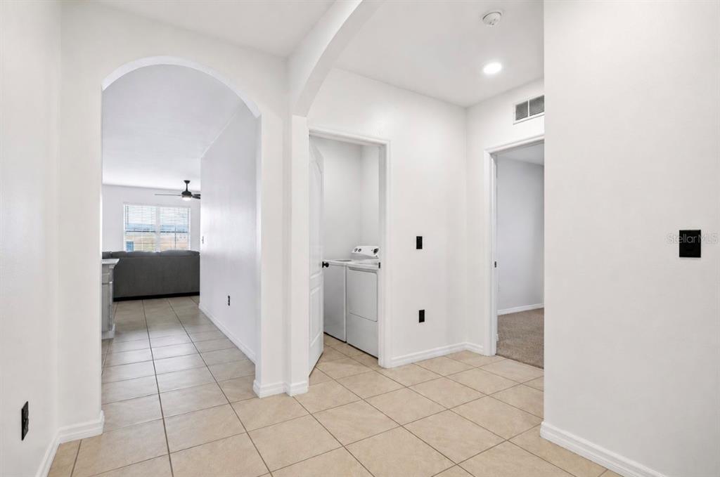 A hallway with tile flooring leads to a laundry closet and an arched living area — 3155 COUNTRY CLUB CIRCLE, WINTER HAVEN, FL
