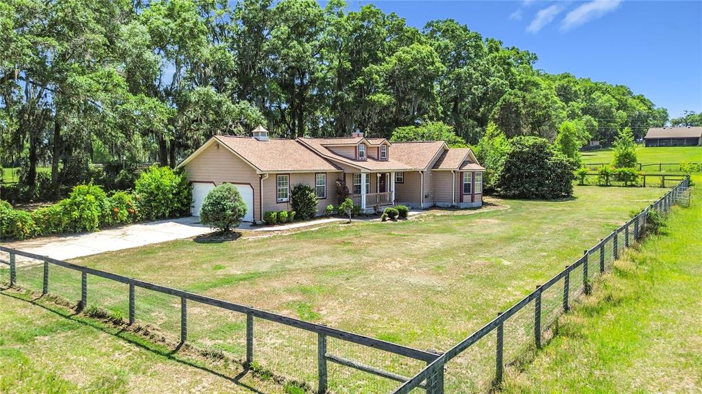 A tan single-story house with a brown roof sits behind a wooden post-and-rail fence — 20540 SW 5TH PLACE, DUNNELLON, FL