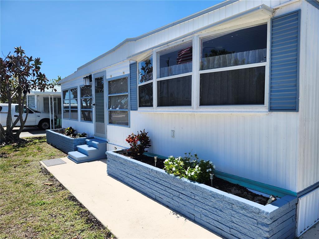 The exterior of a white mobile home features blue shutters, blue brick planters, and concrete steps — 1252 KINGFISHER DRIVE, ENGLEWOOD, FL