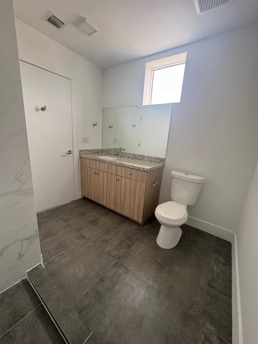 A bathroom features a wood-grain vanity with a granite countertop, a toilet, and tile flooring — 2010 SW 25th Terrace # 305, Miami FL 33133, MIAMI, FL
